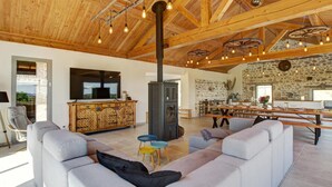 Un vaste espace de vie doté d’un haut plafond, d’une cheminée, d’un mur en pierre et d’un coin repas avec une longue table.