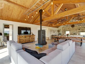 Ein geräumiges Wohnzimmer mit hoher Decke, Kamin, Steinwand und Essbereich mit langem Tisch.