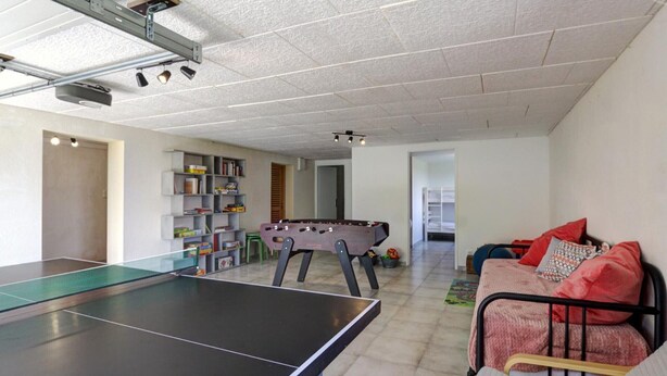 Une pièce avec une table de ping-pong, un baby-foot, une bibliothèque et un lit avec des oreillers.