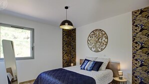 Une chambre à coucher avec un lit, un grand miroir, une décoration murale en forme d’arbre et une fenêtre.
