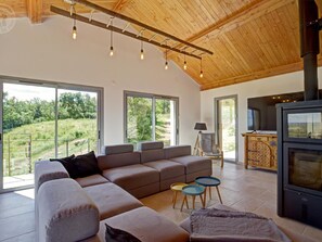 A modern living room with a sectional sofa, a fireplace, and large windows offering a view of the outdoors.