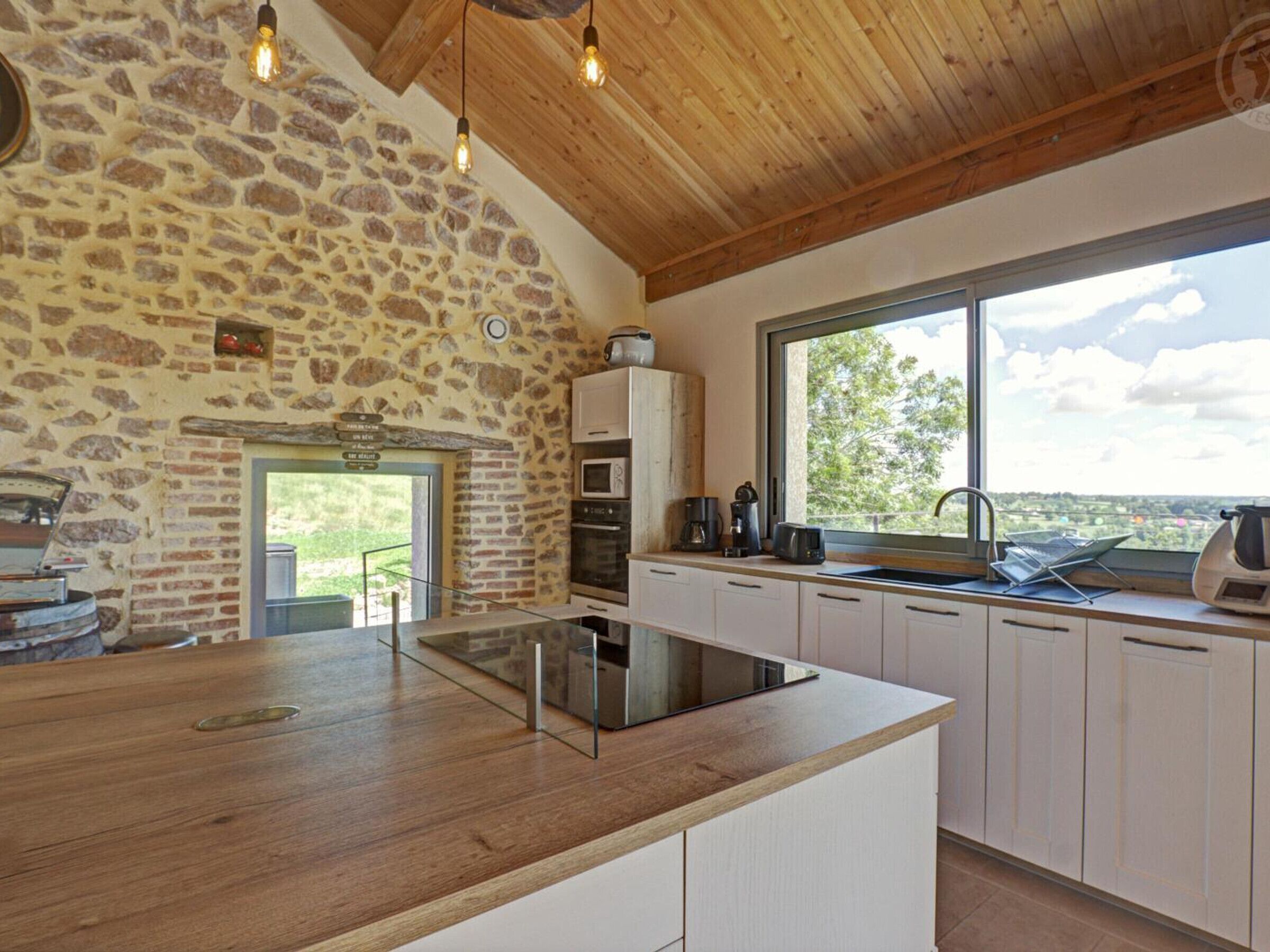 A kitchen with a stone wall, wooden ceiling, and a large window offering a view.