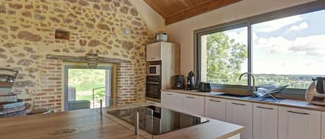 Una cocina con pared de piedra, techo de madera y un amplio ventanal con vistas.
