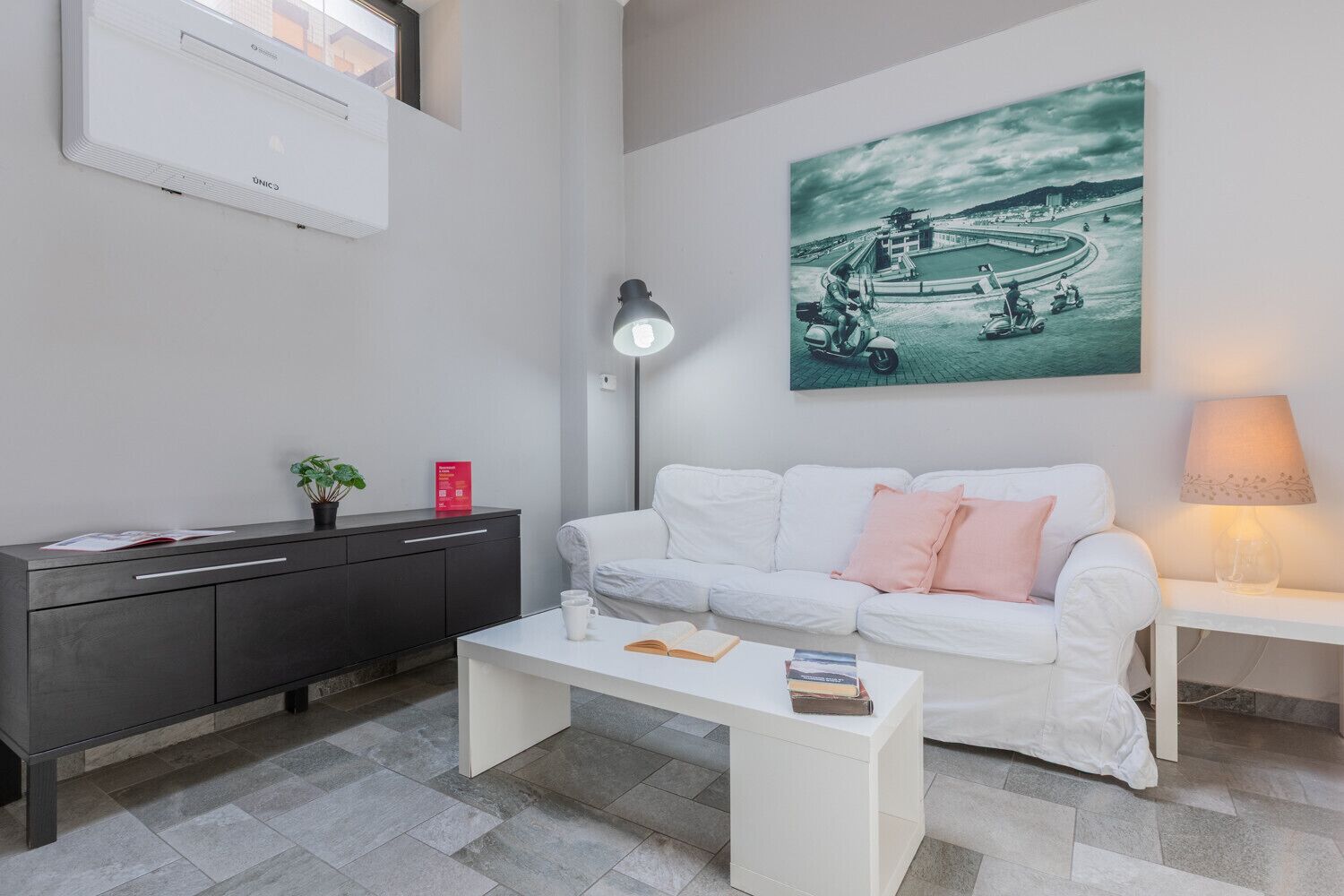 Ein modernes Wohnzimmer mit einem weißen Sofa, einem Couchtisch, einem Schreibtisch und einer Wandklimaanlage.
