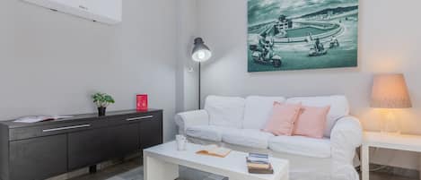 A modern living room with a white sofa, a coffee table, a desk, and a wall-mounted air conditioner.