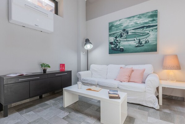 A modern living room with a white sofa, a coffee table, a desk, and a wall-mounted air conditioner. - Loft Lingotto by Wonderful Italy (Turin)