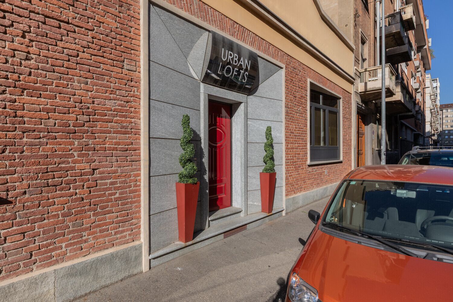 Un edificio de ladrillo con un letrero que dice 'URBAN LOFTS' y dos macetas con plantas en la acera.