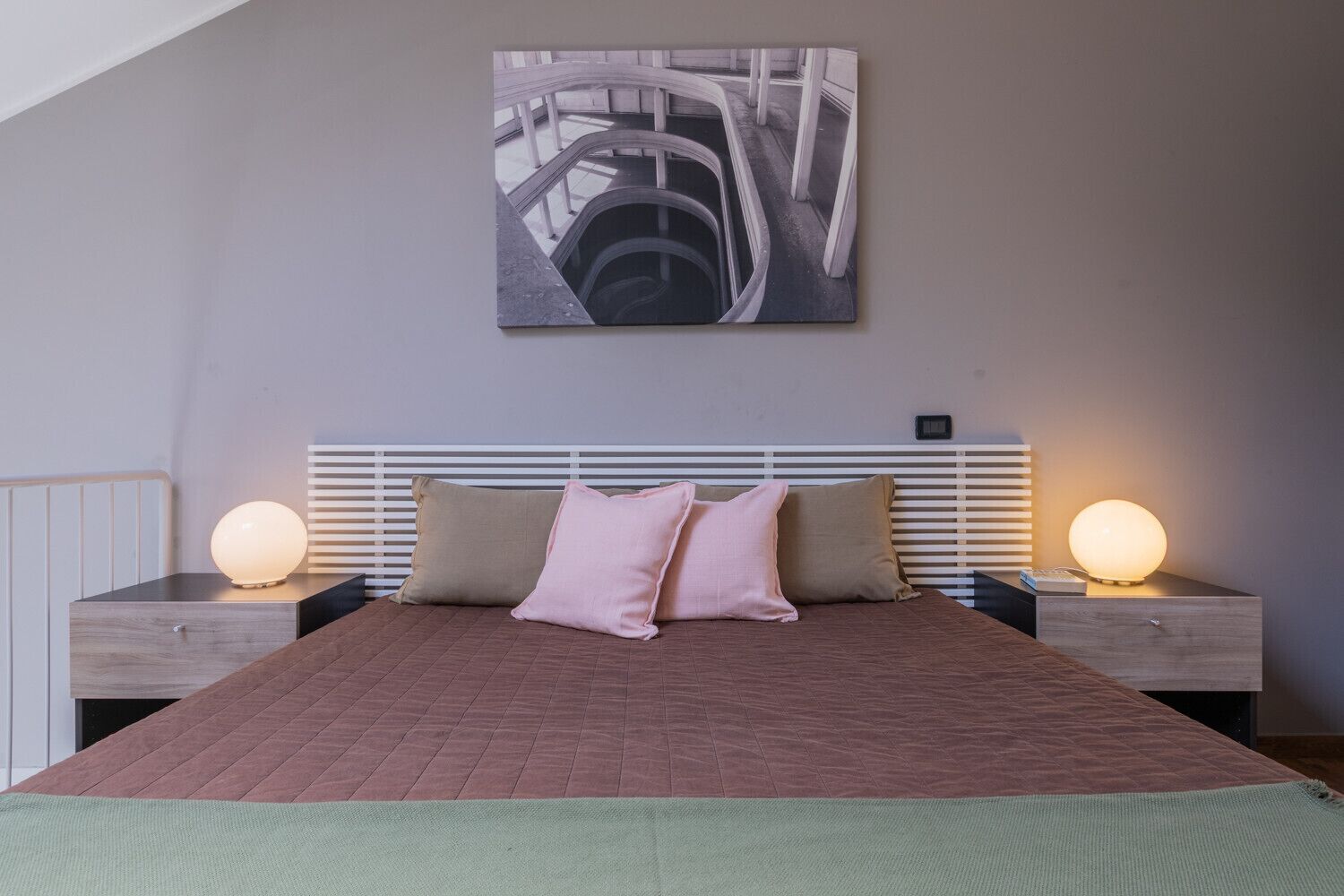 Un dormitorio con una cama, dos mesitas de noche con lámparas, un cabecero y una obra de arte colgada en la pared.