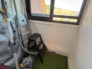 A room with a window, a vacuum cleaner, and a small black stool. - Charming apartment near the sea - 4 guests (Blonville-sur-Mer)