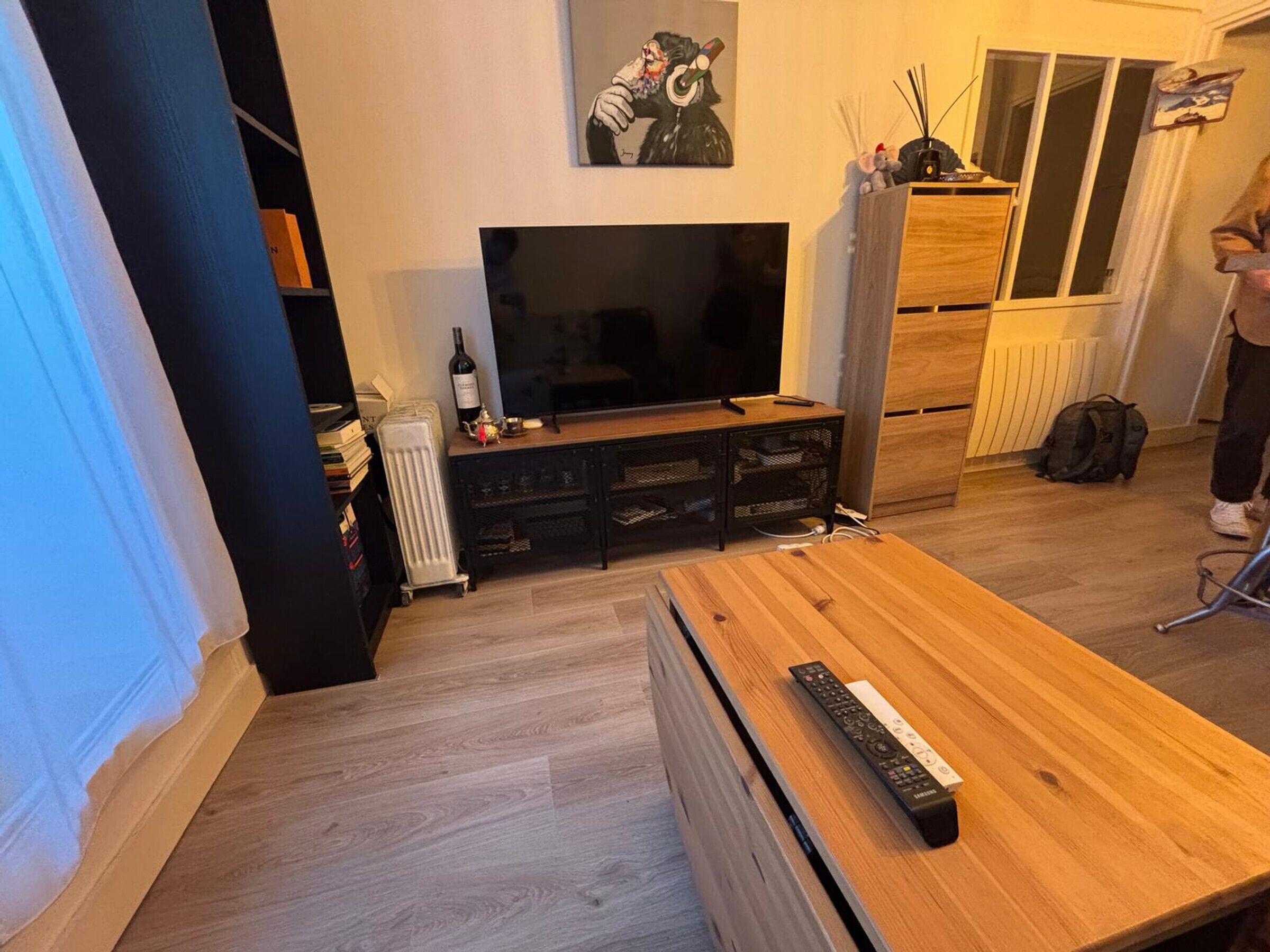 Una sala de estar con televisor de pantalla plana, mueble de entretenimiento de madera y una mesa de centro de madera con un control remoto.