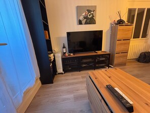 A living room with a TV, wooden coffee table, and a bookshelf. - Charming apartment near the sea - 4 guests (Blonville-sur-Mer)