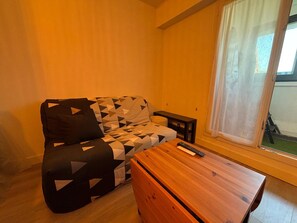 Una habitación con sofá, mesa de madera y ventana con cortinas.