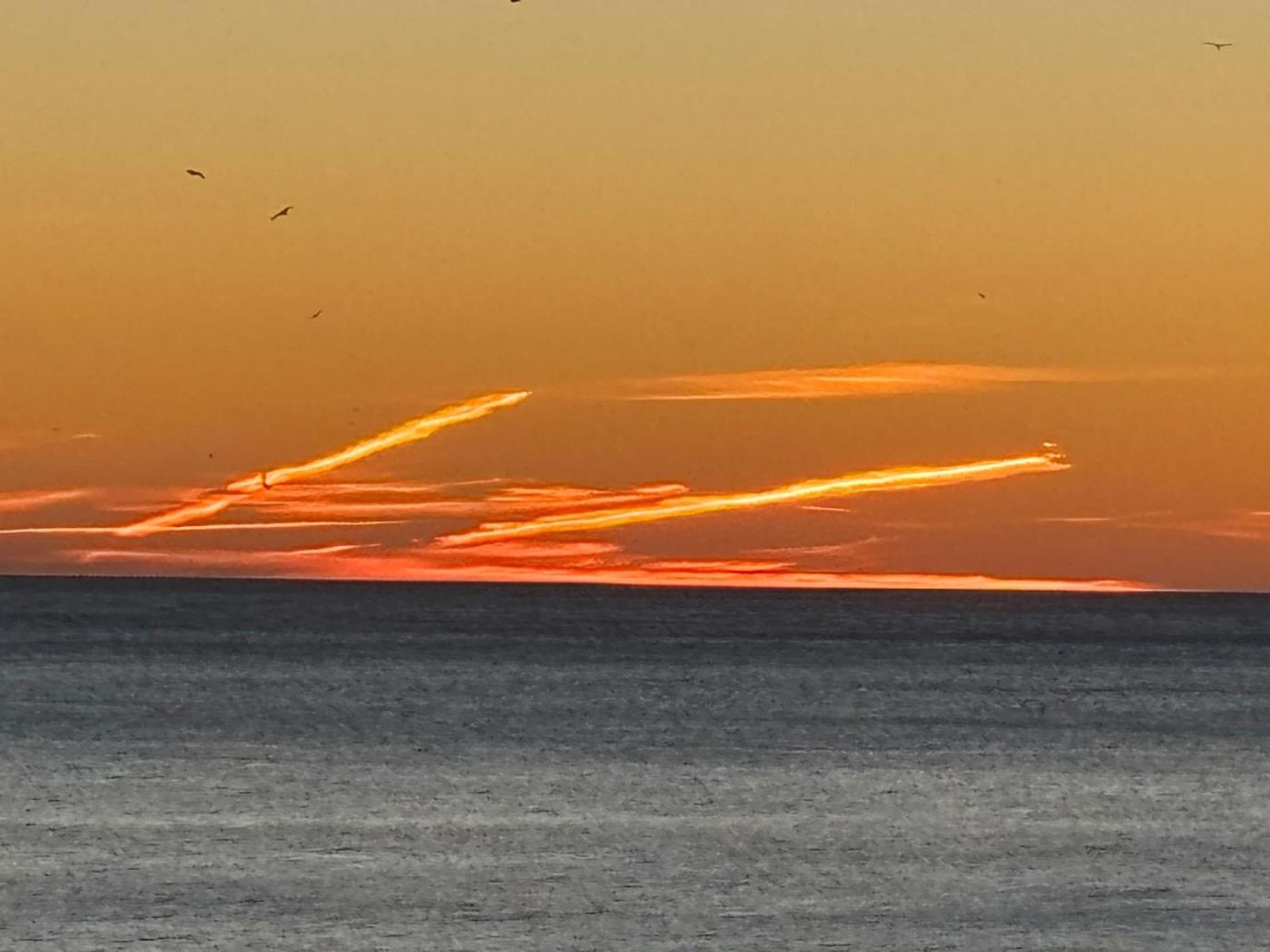 A sunset over a body of water with visible cloud formations.