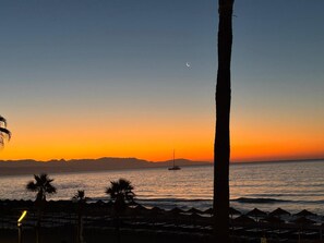 A beach scene with a sunset, palm trees, and a sailboat on the water. - Elegant apartment, sea view, AC - 4 guests (Torremolinos)