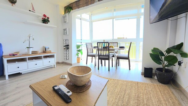 Una sala moderna con una mesa de centro de madera, un televisor montado en la pared y un comedor con sillas y una mesa.