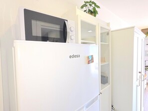 Un réfrigérateur blanc avec un four à micro-ondes sur le dessus, une porte en verre et une petite plante sur l’étagère supérieure.