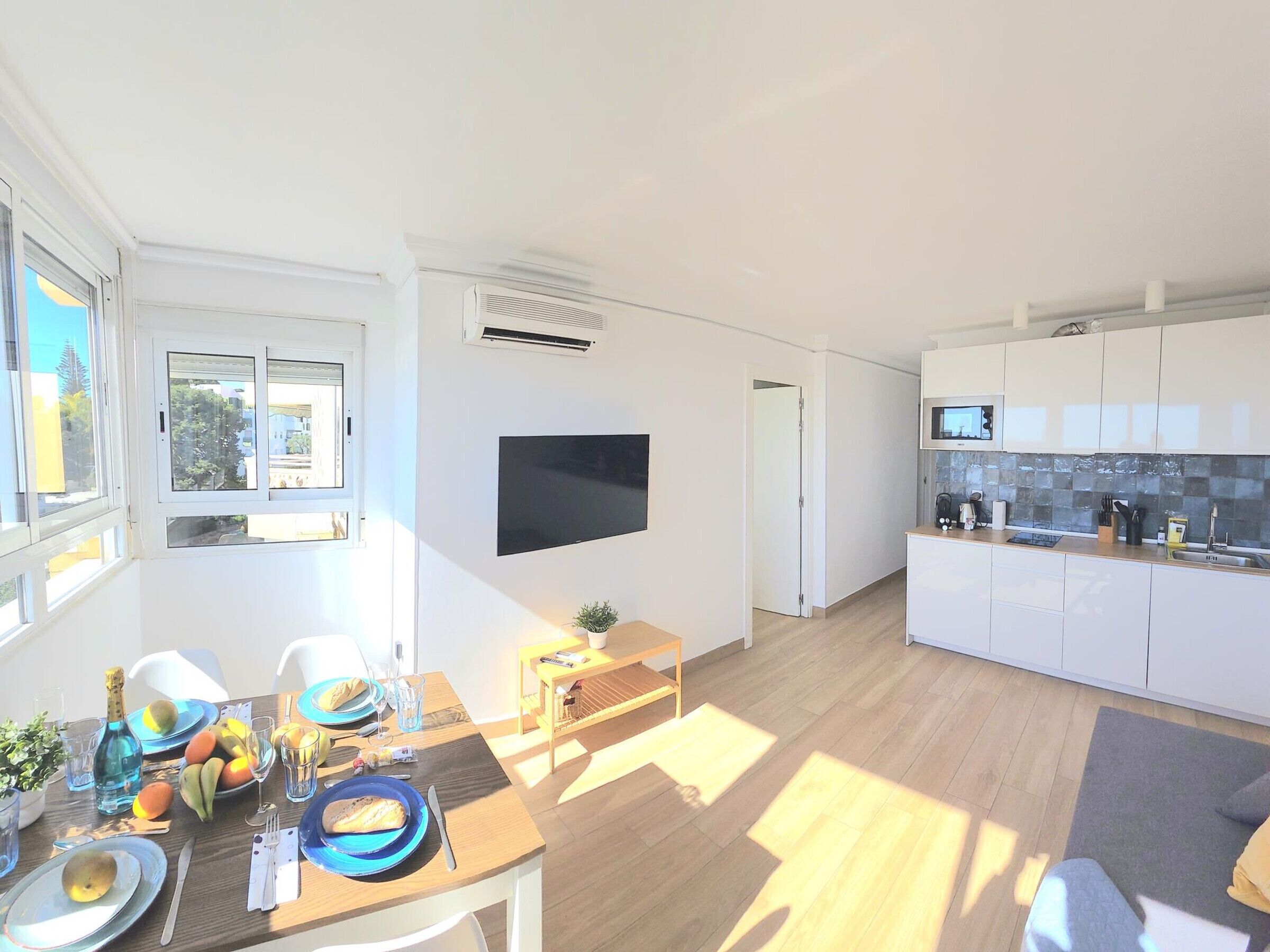 A modern kitchen with white cabinets, a flat-screen TV, and a dining area with a table set for two.
