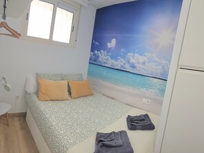 Quarto com cama, televisão na parede, janela e uma mesinha.