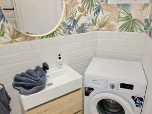 Ein Badezimmer mit einem weißen Waschbecken, einem Handtuch, einer Waschmaschine und einem Spiegel mit Zierrahmen in Blattform.