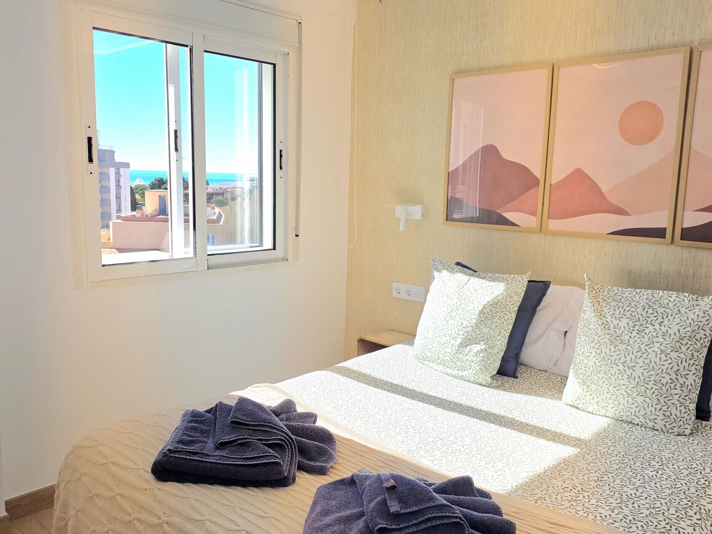 Una habitación de hotel con cama, ventana y vista a edificios, además de un cuadro en la pared.