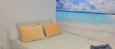 A bed with a patterned bedspread, two pillows, and a view of a beach through a wall mural.
