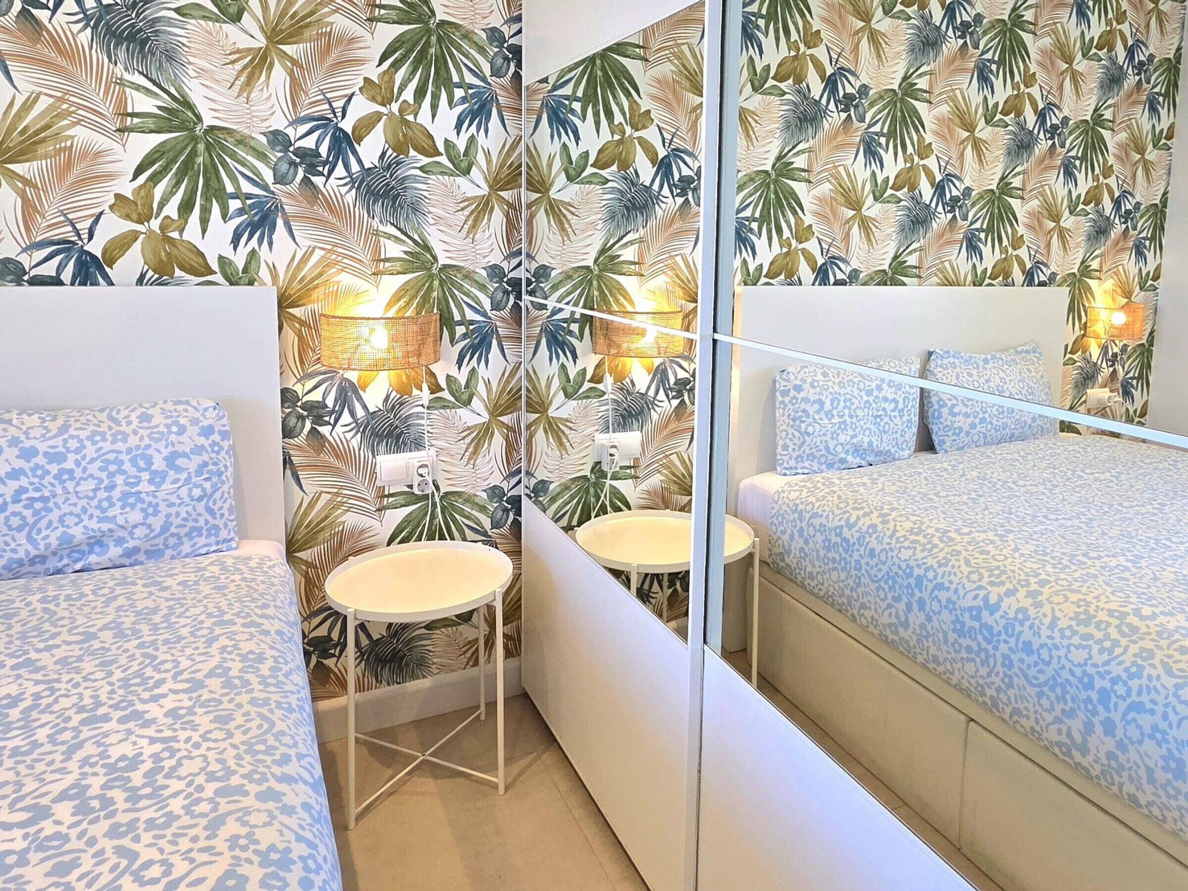 A bedroom with a mirrored wall, a round table, and a bed with a patterned bedspread.
