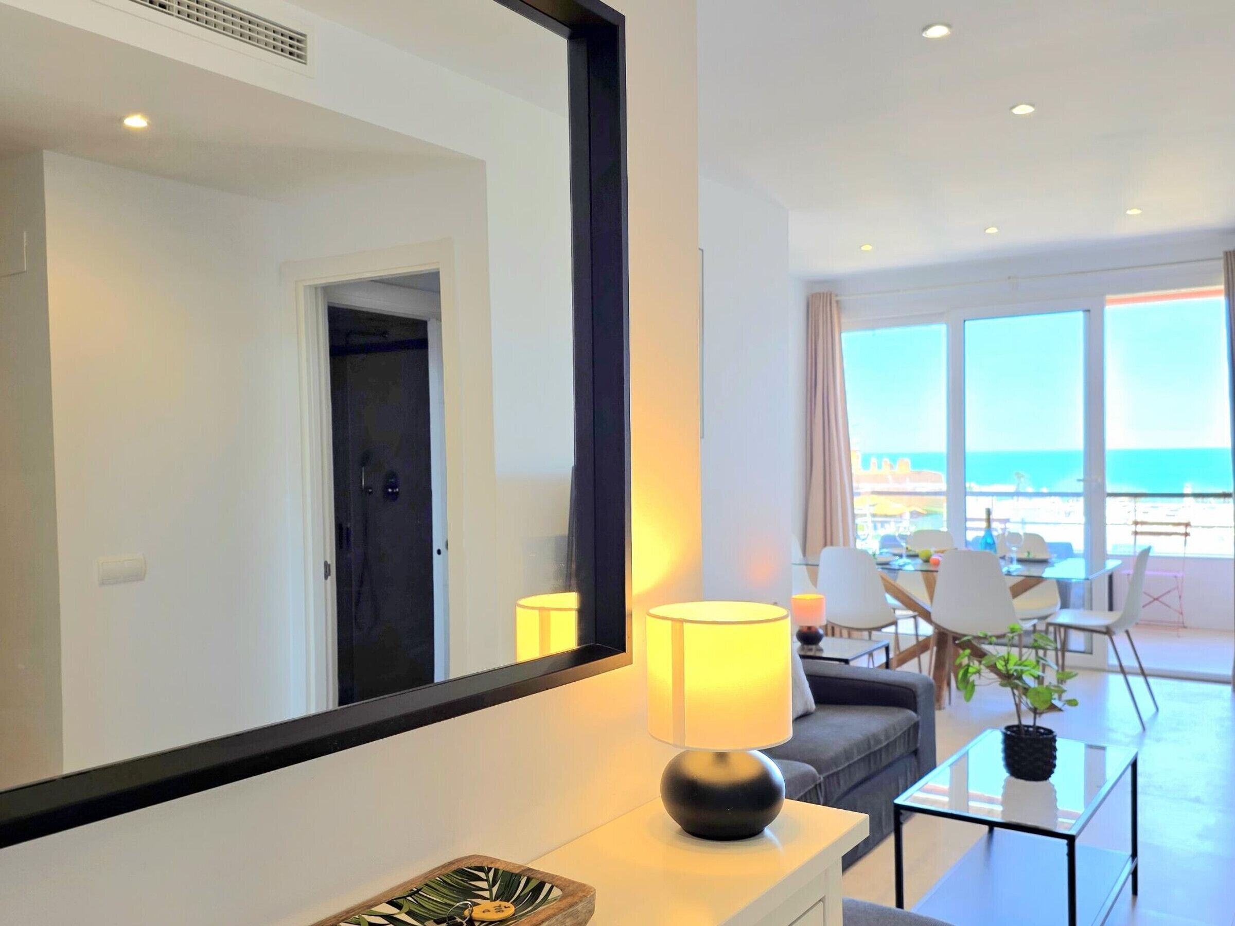 Une chambre d’hôtel moderne, dotée d’un grand miroir, d’un canapé, d’une table basse et offrant une vue sur la mer grâce à de grandes fenêtres.