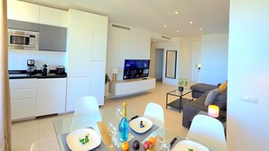 A modern kitchen with built-in appliances, a dining area with a glass table, and a living space with a sofa and a TV. - Apartment sea view, AC & WiFi - 6 guests (Torremolinos)