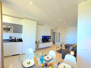 Eine moderne Küche mit eingebauten Geräten, ein Essbereich mit einem Glastisch und ein Wohnbereich mit einer Couch und einem Fernseher.
