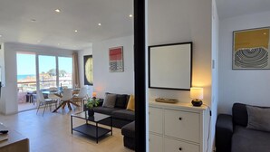 A modern living room with a sofa, a coffee table, and a dining area with chairs and a table. - Apartment sea view, AC & WiFi - 6 guests (Torremolinos)