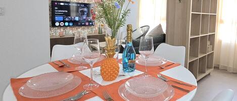 Un comedor con una mesa redonda para cuatro personas, un televisor montado en la pared y una estantería al fondo.
