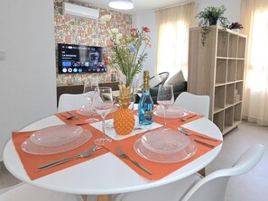 A dining area with a round table set for four, a television mounted on the wall, and a bookshelf in the background. - New central apartment - 2 guests (Benalmádena)