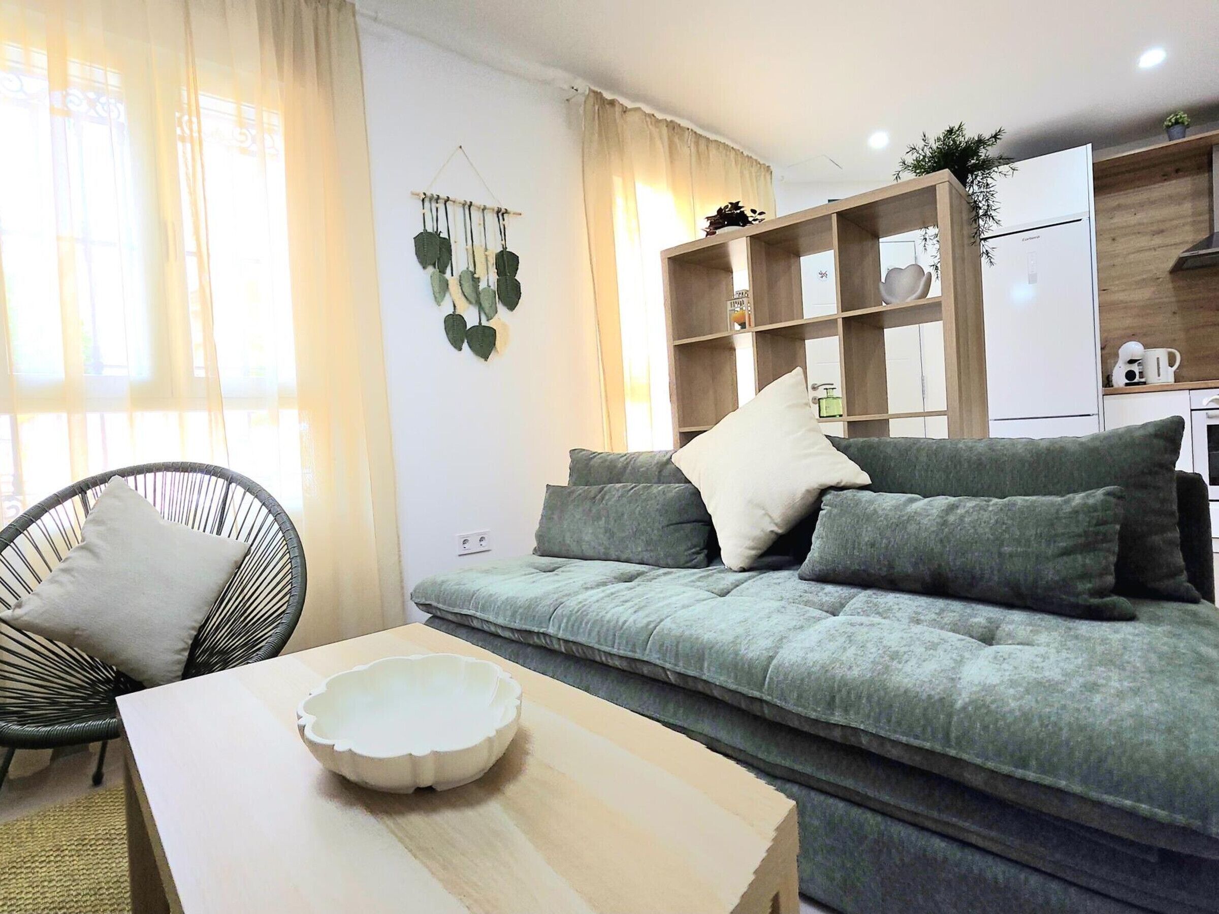 Ein Wohnzimmer mit Sofa, einem Sessel, einem Tisch und einem Küchenbereich im Hintergrund.