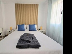 Ein Hotelzimmer mit einem großen Bett, zwei Nachttischen, einem Sessel und einem Fenster mit Vorhängen.