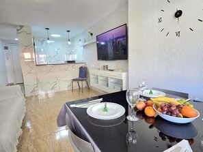 Ein Essbereich mit einem für zwei Personen gedecktem Tisch, einem an der Wand montierten Fernseher und einem Stuhl.
