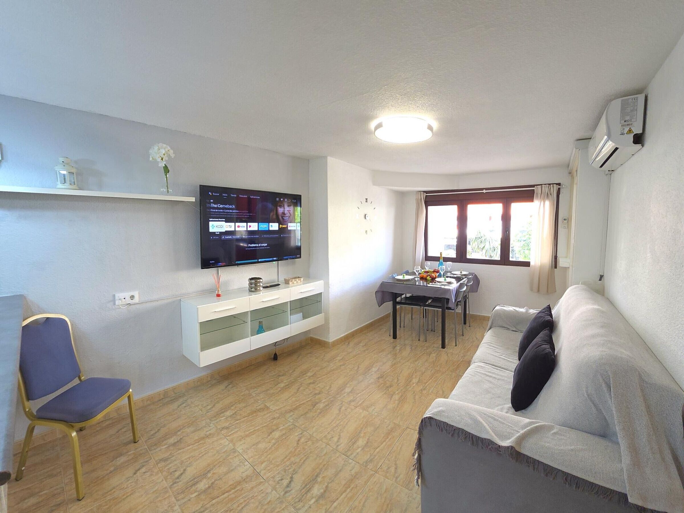 A living room with a flat-screen TV, a dining table with chairs, a sofa, and a window with curtains.
