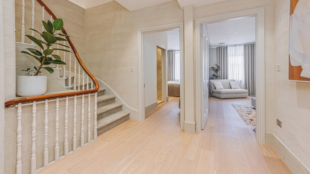 A modern interior with a wooden staircase, a living area with a sofa, and a hallway leading to another room. - Luxury London Six-Bedroom House in Marylebone - Moments from Regent’s  Park (London)