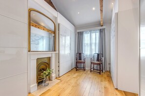 A hallway with a fireplace, two chairs, and a large mirror.