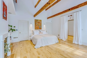 A bedroom with a wooden floor, white walls, a bed with white bedding, a painting above the bed, and a door leading to another room. - Luxury London Six-Bedroom House in Marylebone - Moments from Regent’s  Park (London)