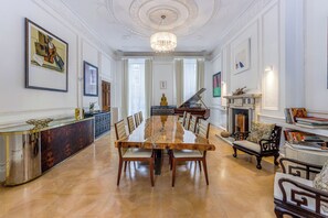 A spacious room with a long wooden dining table, chairs, a piano, and a fireplace. - Luxury London Six-Bedroom House in Marylebone - Moments from Regent’s  Park (London)