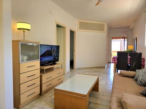 Ein Wohnzimmer mit Fernseher, Holzmöbeln, einem Essbereich mit Stühlen und einem Balkon mit Ausblick.