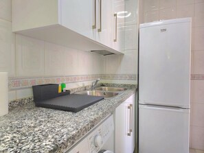 A kitchen with a granite countertop, a stainless steel sink, a white refrigerator, and a black tray with bottles. - Panoramic sea view apartment - 5 guests (Torremolinos)