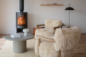 A cozy room with a modern fireplace, a plush armchair, a small table with a book, and a floor lamp.