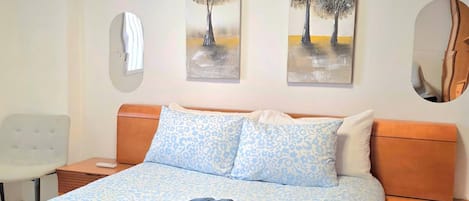 A hotel room with a bed, two wall-mounted paintings, a mirror, and a chair.