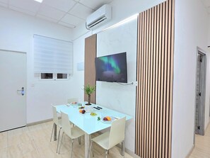 Ein Konferenzraum mit einem weißen Tisch, Stühlen, einem Wand-Fernseher und einem Blumentopf.
