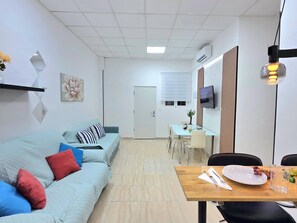 Ein modernes Wohnzimmer mit einer Couch, einem Esstisch und einem an der Wand befestigten Fernseher.