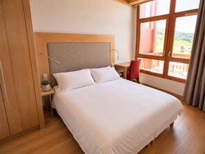 Ein Hotelzimmer mit einem großen Bett, einem Holz-Kopfteil, einem Schreibtisch mit Stuhl und einem Fenster mit Blick ins Freie.