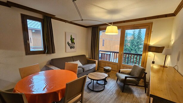 Ett mysigt vardagsrum med ett träbord, en soffa och en balkong med utsikt över träd.