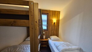 Ett litet rum med två våningssängar, ett litet bord, en lampa och ett fönster med utsikt.