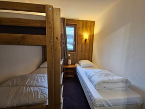 Ein kleines Zimmer mit zwei Etagenbetten, einem Tisch, einer Lampe und einem Fenster mit Blick.